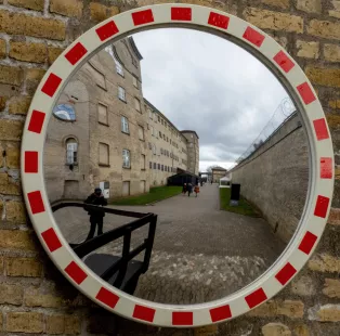 Fotografi av rund spegel. I spegeln syns två personer gå på en innergård, omgivna av höga, ljusa byggnader.