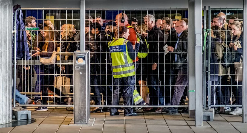Fotografi på människor bakom ett stängsel, taget på Hyllie station i Malmö.